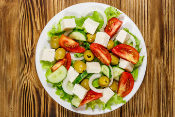 Greek salad with fresh vegetables, feta cheese and green olives on wooden table. Top view