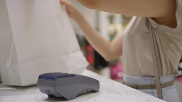 Lockdown arc shot of unrecognizable woman touching credit card onto payment terminal at checkout counter of retail outlet, then taking shopping bags and leaving