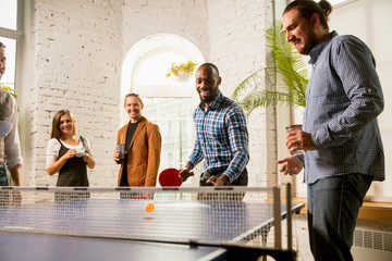 Young people playing table tennis in workplace, having fun. Friends in casual clothes play ping...
