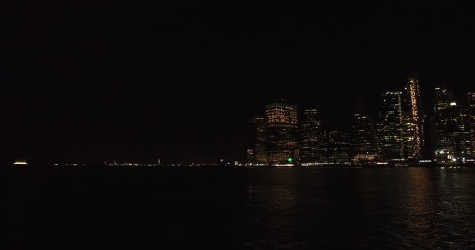 Wide shot of the Upper New York Bay with the skyscrapers of the Financial District of Manhattan at night.