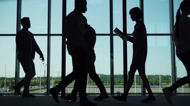 Silhouettes of busy business people with documents and notebooks walking in office lobby while weird carefree man dancing near panoramic window in slow motion