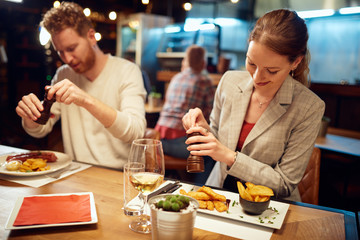 Two beautiful caucasian friends sitting in restaurant and adding salt in served food.
