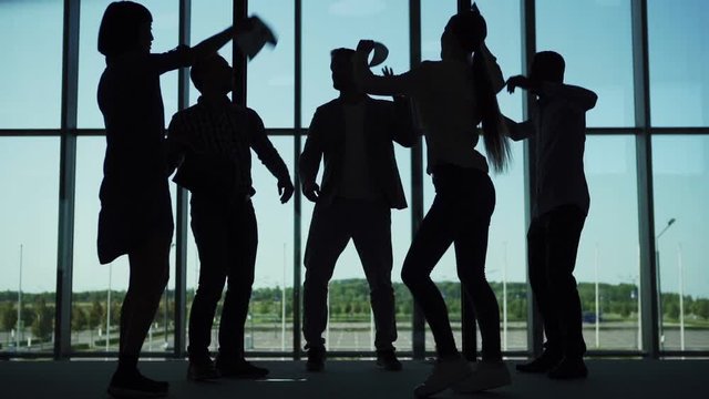 Silhouettes of business people standing in office lobby and discussing issues, then throwing papers and documents away  and dancing joyfully in slow motion celebrating freedom