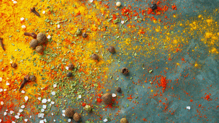 Different spices scattered on the table, red paprika powder, turmeric, salt, cloves, pepper