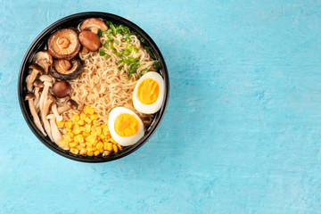 Ramen. Soba with eggs, mushrooms, and vegetables, shot from the top on a blue background with a place for text