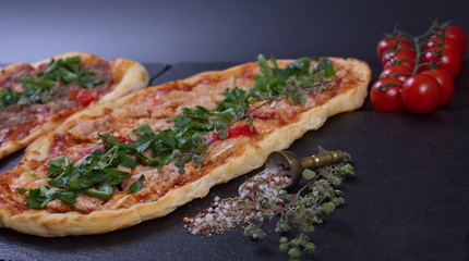 Turkish pizza with chicken breast, meat and vegetables lies next to spices on a dark background