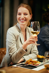 Portrait of beautiful caucasian brunette dressed elegant posing with glass of wine while sitting in restaurant with her friends.