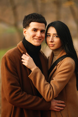 Stylish young couple outdoors on a beautiful autumn day in the forest. Young couple in love holding hands and walking through a park on a  autumn day. The concept of youth, love and lifestyle.