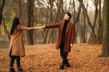 Stylish young couple outdoors on a beautiful autumn day in the forest. Young couple in love holding hands and walking through a park on a  autumn day. The concept of youth, love and lifestyle.