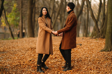 Stylish young couple outdoors on a beautiful autumn day in the forest. Young couple in love holding hands and walking through a park on a  autumn day. The concept of youth, love and lifestyle.