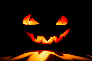 Fototapeta premium Halloween pumpkin smile and scary eyes for party night. Close up view of scary Halloween pumpkin with eyes glowing inside at black background. Selective focus