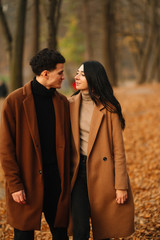 Stylish young couple outdoors on a beautiful autumn day in the forest. Young couple in love holding hands and walking through a park on a  autumn day. The concept of youth, love and lifestyle.