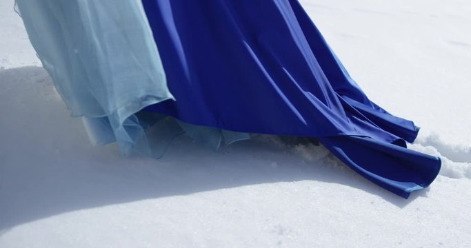 Woman in blue dress is walking through snowland. Footprints on the snow and hem clouseup.