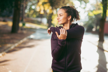 Portrait of sportswoman warming herself up for training. Beautiful woman in sportswear outdoors working out.