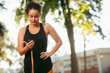 Beautiful young woman looking at stopwatch. Female athlete training in park.