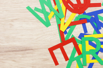colorful jumbled letters, made of paper,  lying on wood
