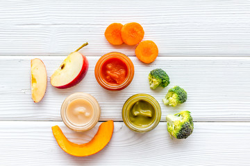 Baby food. Colorful puree in glass jars near vegetables and fruits on white wooden background top view