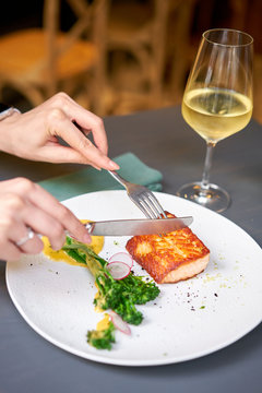 Lunch in a restaurant, a woman cuts the Salmon steak fillet and garnished with young broccoli. Restaurant menu, a series of photos of different dishes