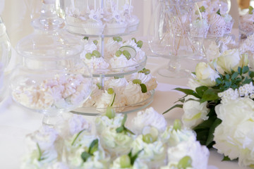 Candy bar: table with a white tablecloth, glassware, cakes, sweets, macaroons, marshmallows, cream, grapes