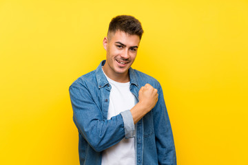 Young handsome man over isolated yellow background celebrating a victory