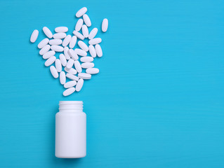 Pills and white bottle on blue background.