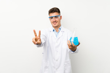 Young scientific holding laboratory flask over isolated background smiling and showing victory sign