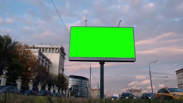 Empty billboard with a green screen for advertising, on a busy street, blank billboard at sunset in city on roadside against cars