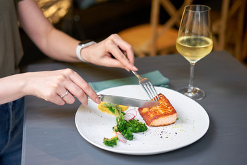 Lunch in a restaurant, a woman cuts the Salmon steak fillet and garnished with young broccoli. Restaurant menu, a series of photos of different dishes