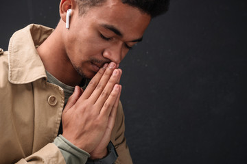 Image of african american guy using earpods and holding palms together