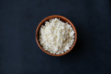 Cottage cheese in a brown bowl on a dark background. Dietary food with calcium.