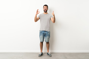 A full-length shot of handsome man with beard showing ok sign and thumb up gesture © luismolinero