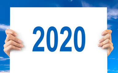 Hands holding a white board with 2020, blue sky background