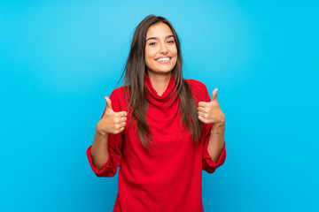 Young woman with red sweater over isolated blue background giving a thumbs up gesture