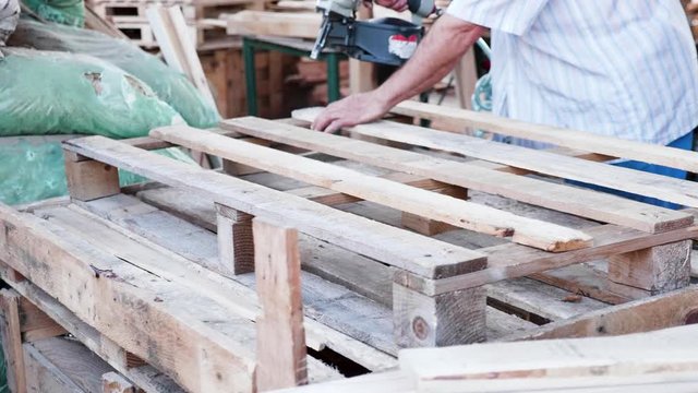 Man Worker in a timber factory using a nail gun to make a wooden pallet