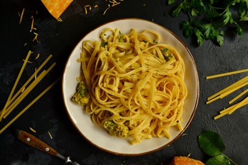 Spaghetti in a beautiful plate on a dark background. Appetizing pasta with broccoli. Noodles with cream and cheese. Homemade noodles.