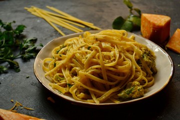 Spaghetti in a beautiful plate on a dark background. Appetizing pasta with broccoli. Noodles with cream and cheese. Homemade noodles.
