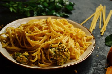Spaghetti in a beautiful plate on a dark background. Appetizing pasta with broccoli. Noodles with cream and cheese. Homemade noodles.