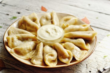Dumplings in a beautiful plate. Dumplings on a wooden background. Wooden table background with autumn leaves. Appetizing little pie with filling. Traditional homemade food.