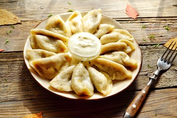 Dumplings in a beautiful plate. Dumplings on a wooden background. Wooden table background with autumn leaves. Appetizing little pie with filling. Traditional homemade food.