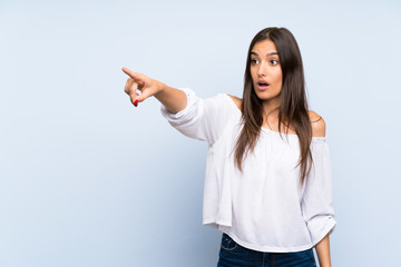 Young woman over isolated blue background pointing away