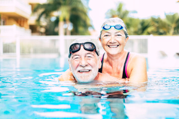 two seniors or mature people together hugged in the blue water of the swimming pool - active woman...