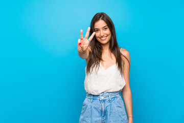 Young woman over isolated blue background happy and counting three with fingers - obrazy, fototapety, plakaty