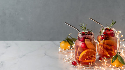 Winter sangria on dark christmas holiday background. Jugful of sangria and glasses with fruit slice, cranberry and rosemary. Copy space for text or design. Horizontal banner. Decoration lighting chain