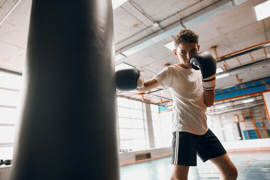 little young hardworking boxer learning to blow the punching bag at sport center, close up photo, effective training process, kid taking up a new hobby