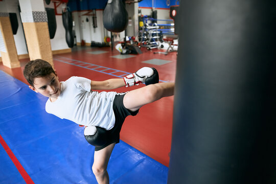serious sweaty boy kicking punching bag at sport center. close up photo. hobby, interest , lifestyle, free time, spare time