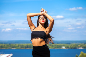 Portrait of a young beautiful girl in a black skirt and a bra posing on a background of blue sky