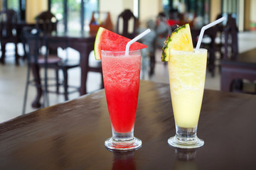 Watermelon and pineapple shakes close up, sliced fruits pieces, straw, two fruit shakes with garnish in transparent glasses on table in bar, cold tropical refreshment drink, healthy natural beverage