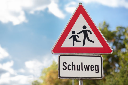 A triangular red and white warning sign depicting running children. It is a way to school. Translation on the sign: way to school.