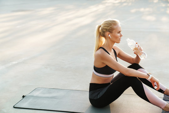 Image of sportswoman in tracksuit drinking water during workout outdoors