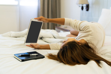 Attractive smiling woman relaxing lying in bed using tablet.